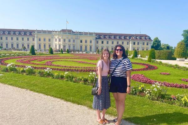 Two women posing in front of historic palace and formal gardens