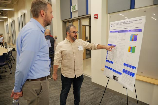 Researcher presenting research poster about Arrhenius rate and material response to conference attendee in modern academic building